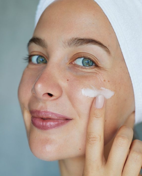 Morning skin care routine. Young beautiful woman is applying  a cream, scrub beauty product on her face. Domestic daily skincare